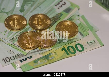 five golden bitcoins lying on many 100 euro bills detail view Stock Photo
