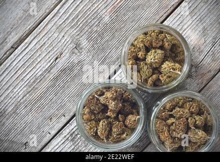 Dry and trimmed cannabis buds stored in a glas jars on a wooden table Stock Photo