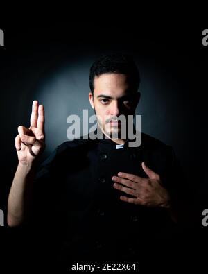 young man dressed in black with chef's clothes looks like a priest who peddles. Spiritual concept. cooking concept. Stock Photo