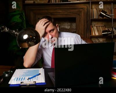Tired frustrated man holding his head while looking at the laptop. Late online business meeting. Stock Photo