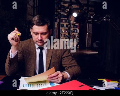 A man in suit works late at night with business documents in his office. Stock Photo