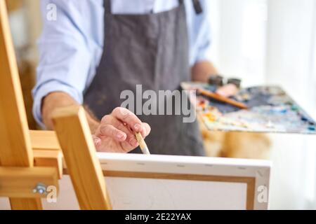 artist applying paint on canvas with paintbrush, his mind full of imagination, creative painter during work. close-up, focus on hands Stock Photo