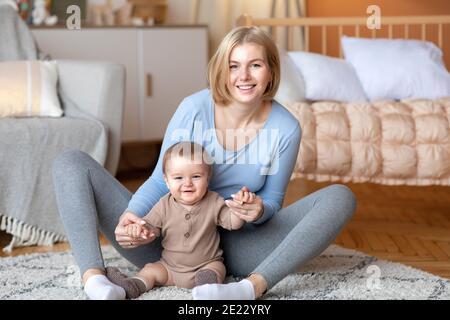 Mother playing with her infant child, sitting on bed Stock Photo