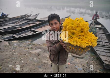 A boy carrying a basket of flowers. Farmers from rural areas bring their vegetables on boat to the nearest market on a foggy winter morning. Sylhet, Bangladesh. Stock Photo