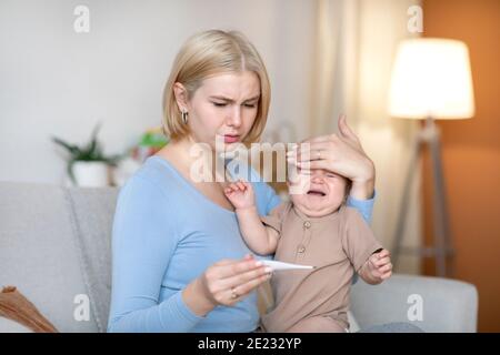 Worried mother takes temperature to sick crying baby at home Stock Photo