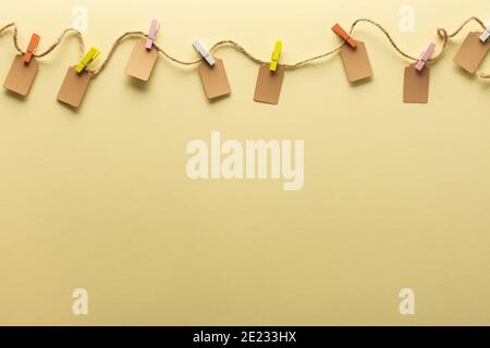 Paper tags tied with colored clothespins to jute rope, rope with tags on trendy yellow background Stock Photo