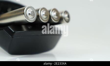 Rechargeable alkaline batteries in a battery charger on a white background. AA fast charger in black. The battery is charging Stock Photo