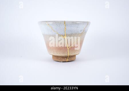 Japanese Kintsugi beige tea cup, gold cracks on antique pottery. Stock Photo