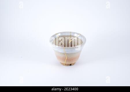 Japanese Kintsugi beige tea cup, gold cracks on antique pottery. Stock Photo