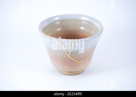 Japanese Kintsugi beige tea cup, gold cracks on antique pottery. Stock Photo