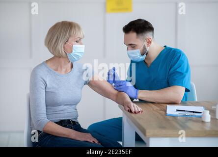 Senior lady being vaccinated against coronavirus at clinic, participating in antiviral campaign Stock Photo