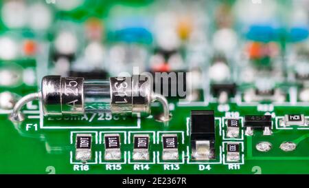 Electrical glass tube fuse or resistors, diode and transistor on printed circuit board in artistic detail. Small safety device soldered to green PCB. Stock Photo