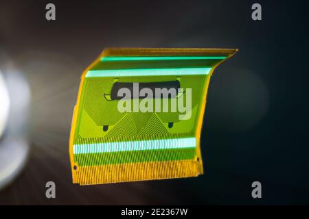 Green flexible circuit board floating on black background. Small bent plastic flex PCB for signals transmission in LCD screens of electronic devices. Stock Photo