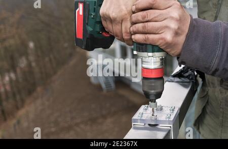 Cordless drilling machine in workman hands. Jig bushing of aluminum and acrylic glass. Steel handrail fixing detail. Drill bit guide template close-up. Stock Photo