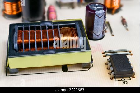 Copper wire winding in transformer rectangular core, integrated circuit, capacitor and inductors. Electronic components on PCB detail. Electrotechnics. Stock Photo