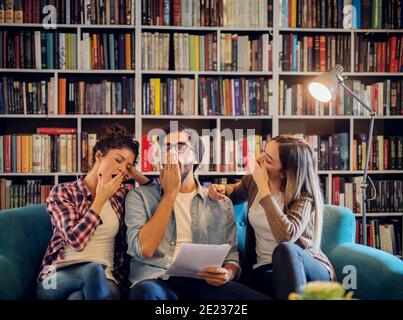 Picture of three young modern student sitting in library. Being tired from learning and preparing exams. Stock Photo