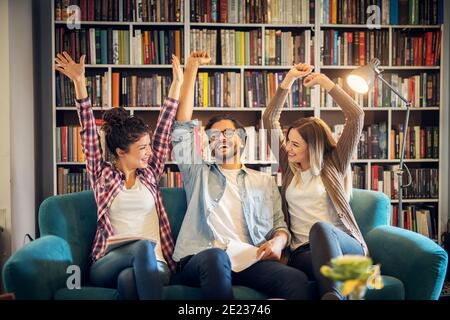 Three happy smiling students celebrating last day of school in library. Stock Photo