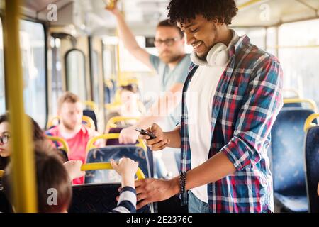 Young Afro-American with headset around his neck is looking at his phone while riding in a bus. Stock Photo