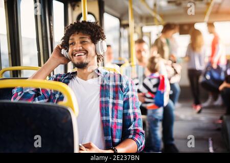 Young Afro-American man is sitting in a bus with headset on his head and listening to the music. Stock Photo