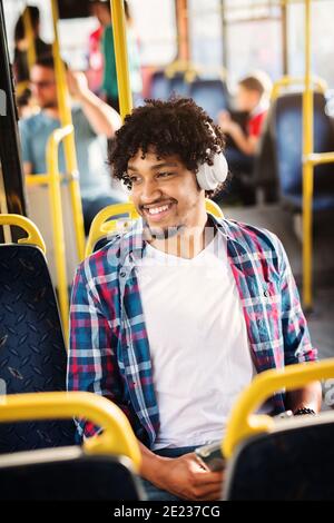 Young Afro-American man is sitting in a bus with headset on his head and listening to the music. Stock Photo