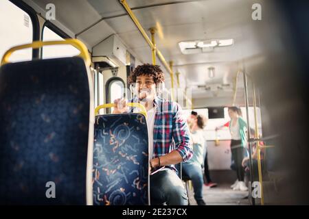 Young beautiful Afro-American man is sitting alone in a bus full of people. Stock Photo