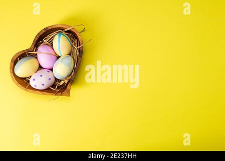Colorful easter eggs in wooden plate on yellow background. Stock Photo