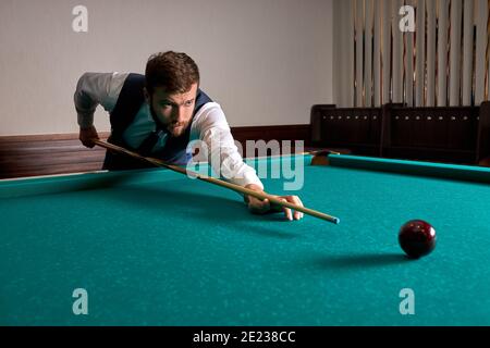 man is playing snooker, he is aiming to shoot the snooker ball. handsome guy holds hands on snooker table. billiards Stock Photo
