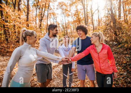 Small group of runners putting hands on hands and smiling. Woods in autumn exterior. Teamwork concept. Stock Photo