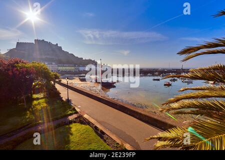 Image of Gorey Harbour with fishing and pleasure boats, the pier bullworks and Gorey Castle in the background with blue sky. Jersey, Channel Islands, Stock Photo