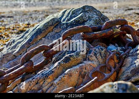 Abstract image of old rusty chains over a granite rock on beach with a shallow depth of field, selective focus. Stock Photo