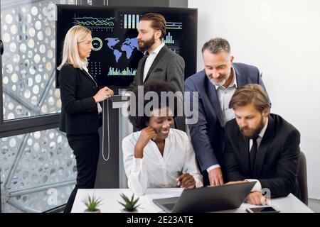 Positive purposeful multiracial business colleagues, working together over joint business project. Focus on mature blond woman and bearded man behind Stock Photo