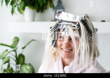 Beautiful young woman with foil on her hair. Bleaching or dyeing process at home Stock Photo