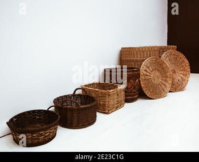 Many wicker straw and bamboo baskets in row with handle and cap on white floor, interior storage containers concept Stock Photo