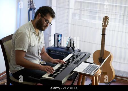 Talented concentrated Hispanic male musician sitting and playing electronic piano in a studio Stock Photo