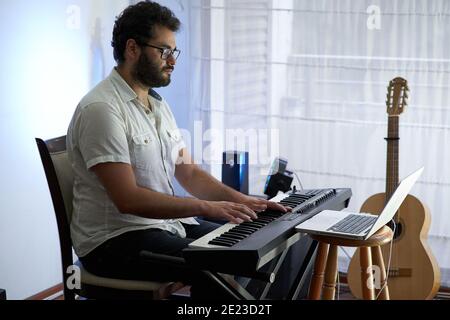 Talented concentrated Hispanic male musician sitting and playing electronic piano in a studio Stock Photo