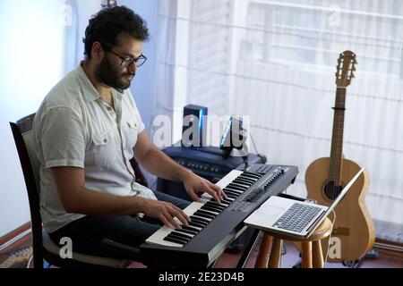 Talented con Hispanic male musician sitting and playing electronic piano in a studio Stock Photo