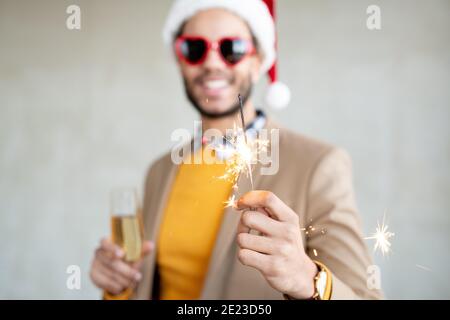 Hand of happy young businessman in Santa cap and heartshaped sunglasses holding flute of sparkling bengal light at xmas party Stock Photo
