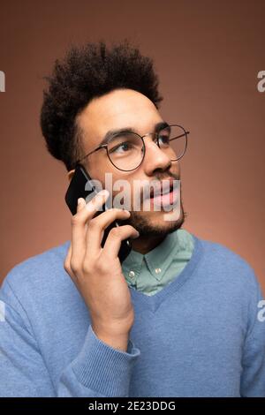 Young mixed-race businessman in eyeglasses and smart casualwear holding smartphone by his ear during business call Stock Photo