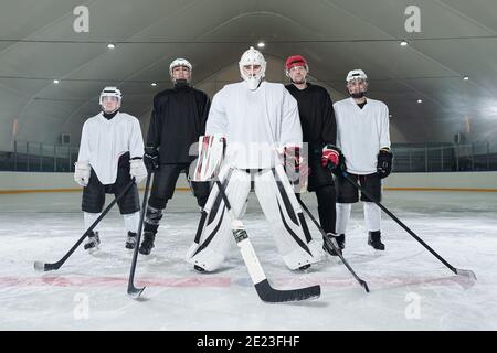 Professional hockey players and their trainer in sports uniform, gloves, skates and helmets standing on ice rink and waiting for start of play Stock Photo