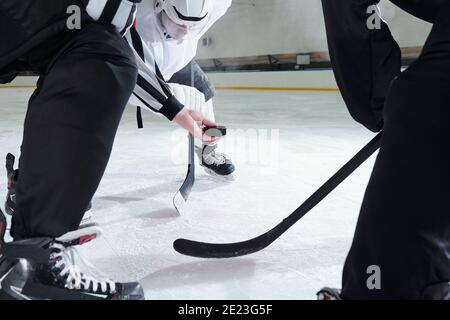 Hockey referee holding puck over ice rink while two rivals with sticks bending forwards and waiting for moment to be the first to shoot it Stock Photo