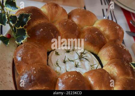 Baked camembert with rosemary sprigs in homemade brioche dough with golden crust. French bread and soft cheese with runny middle are treat for sharing Stock Photo