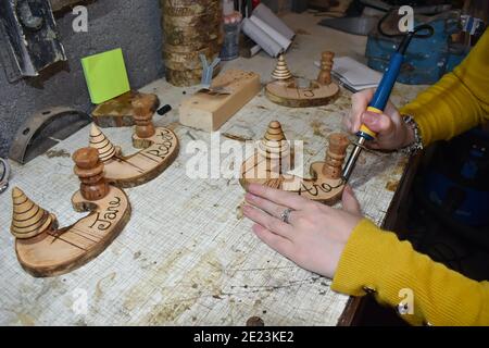 Young woman wearing yellow jumper engraving wooden name tags in a workshop using soldering iron pen. Personalised labels for sorting the table sitting Stock Photo