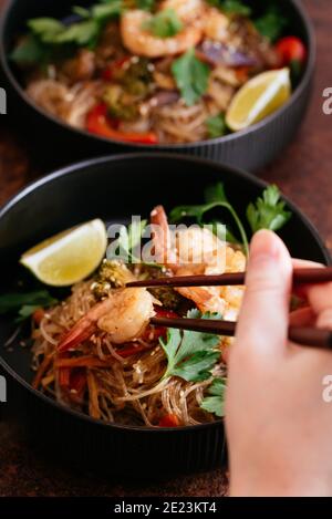 Stir fried noodles with shrimps and vegetables in a wok on dark table, top view Stock Photo