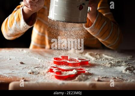 a child using a flour sifter over a cutting board and cookie cutters Stock Photo