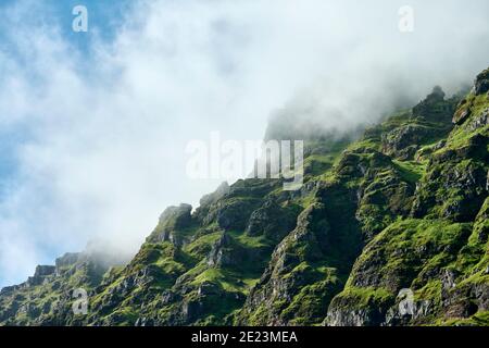 From below of moss covered rocky slope of remote mountain range in foggy cloud in sunshine Stock Photo