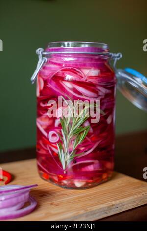 Homemade sweet and spicy pickled red onions sliced in a large glass jar, with the ingredients beside on a wooden cutting board with chili peppers, gar Stock Photo