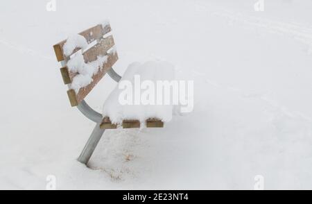 empty snow covered bench viewed from the side isolated in a ghostly winter fog with copy space Stock Photo