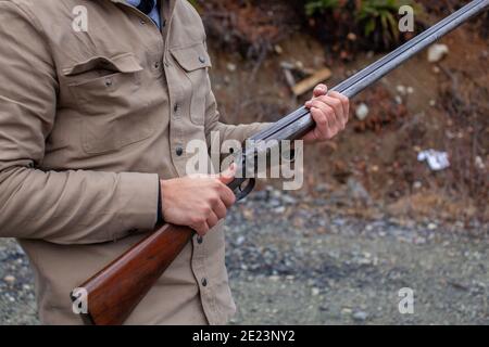 A man holds an old, antique, double-barrel shotgun to his waist, pointing the barrel downrange, ready to load. Outdoor range in Squamish, British-Colu Stock Photo