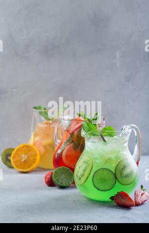Different color lemonade in glass decanters with fruits and garnished with fresh mint and sliced fruits Stock Photo