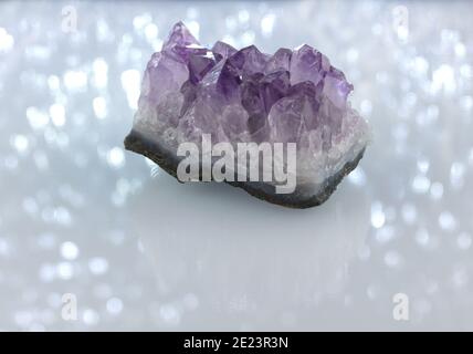 a raw amethyst crystal cluster, mineral specimen on a white sparkly, shimmering background with reflection and copy space Stock Photo